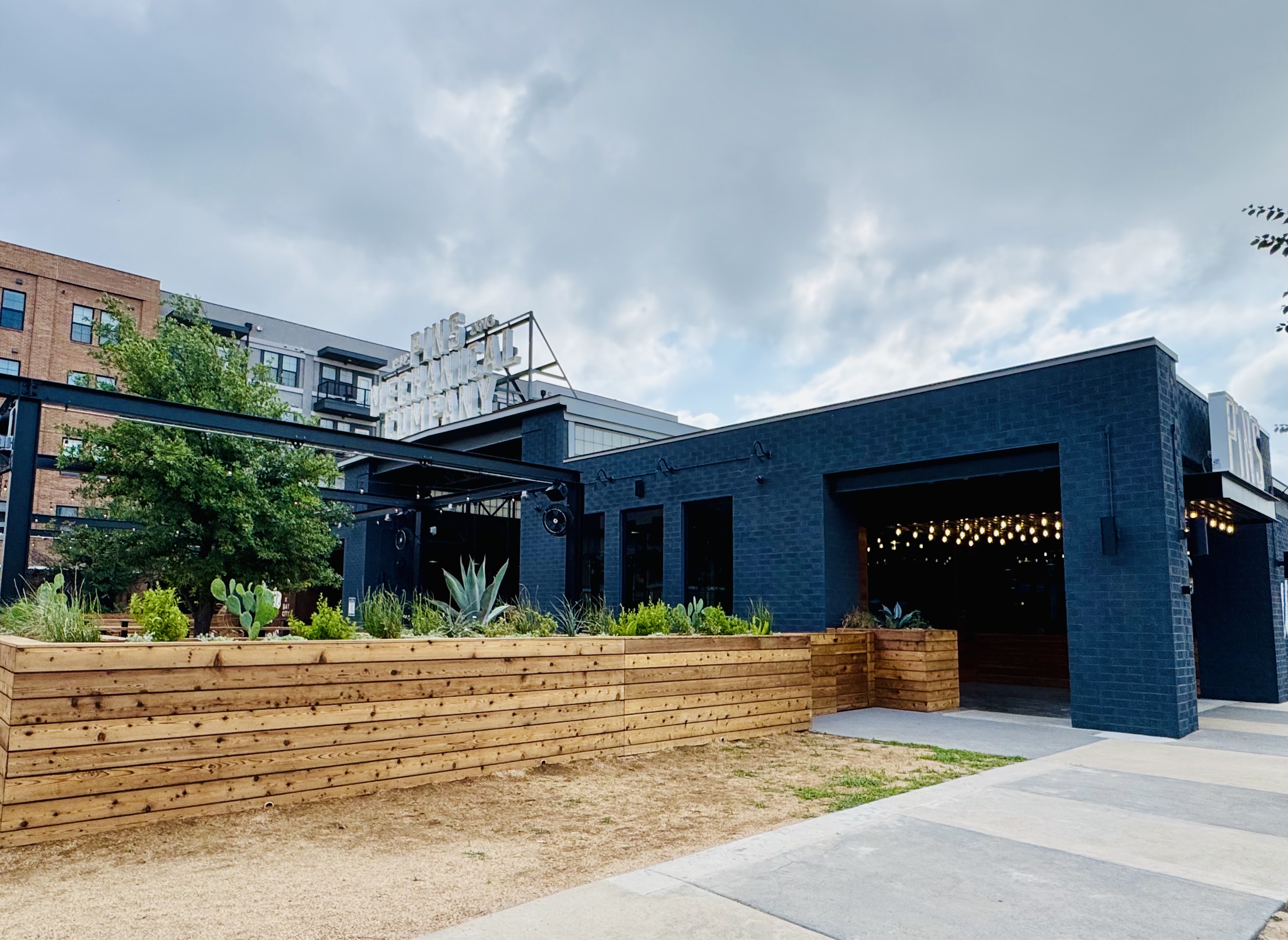 Pins Mechanical at dusk — cedar planter walls against blue-black brick